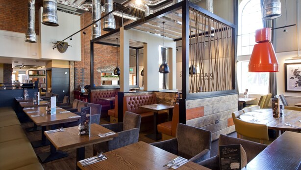 A restaurant with wooden tables, cushioned booths, and hanging pendant lights. - Premier Inn Gloucester - Quayside (Gloucester)