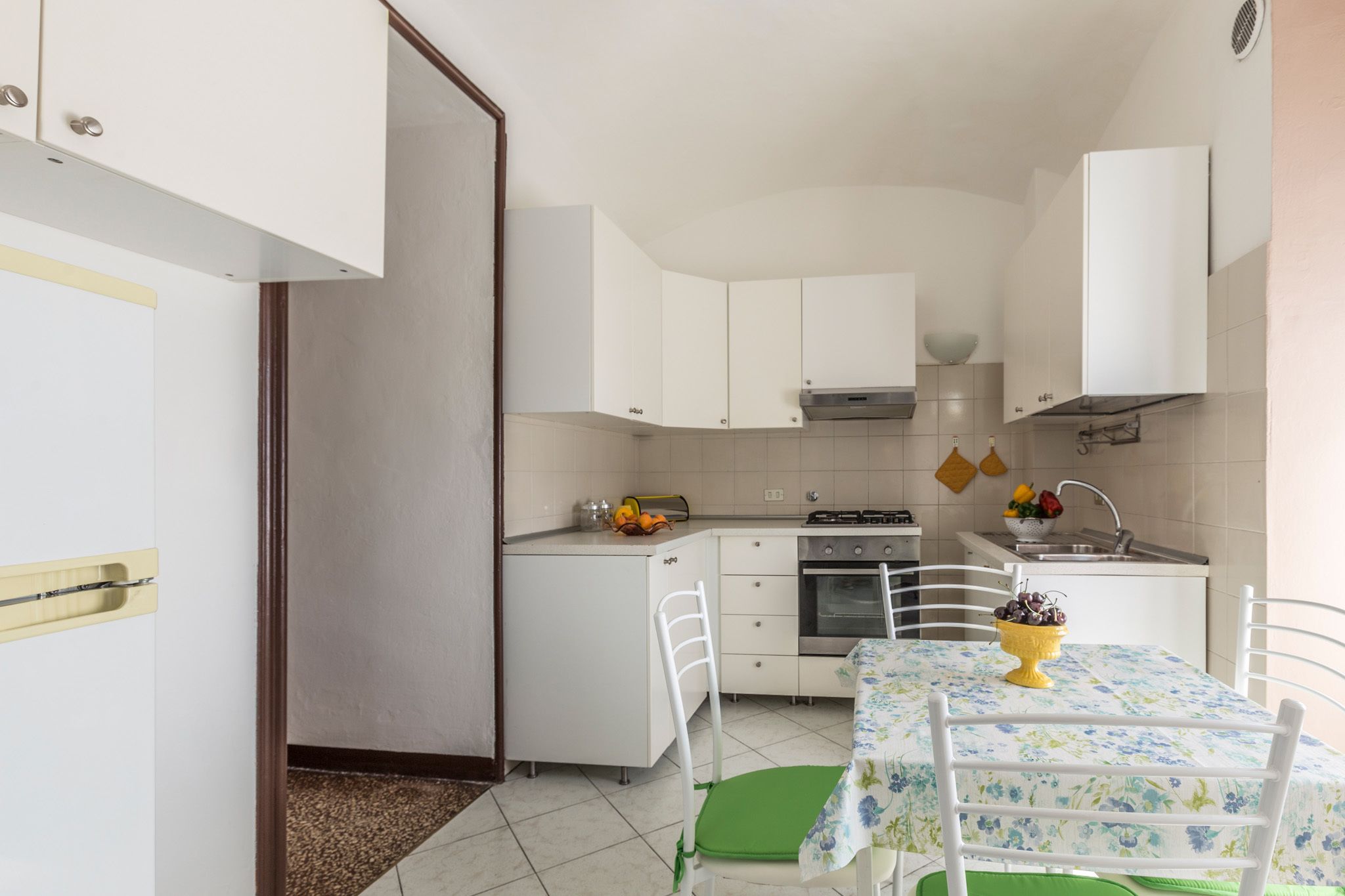 A compact kitchen with white cabinets, a dining table with a floral tablecloth, and a green chair.