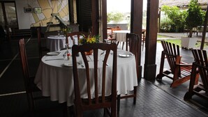 A restaurant with round tables, wooden chairs, and a white tablecloth. - Hostellerie De La Sanaga (Edea)