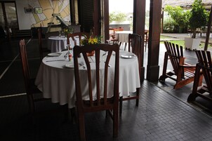 Restaurante com mesas redondas, cadeiras de madeira e toalha de mesa branca.