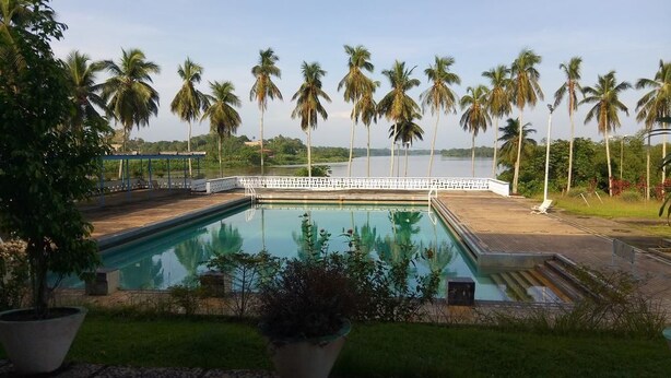 A swimming pool with a view of palm trees and a body of water. - Hostellerie De La Sanaga (Edea)