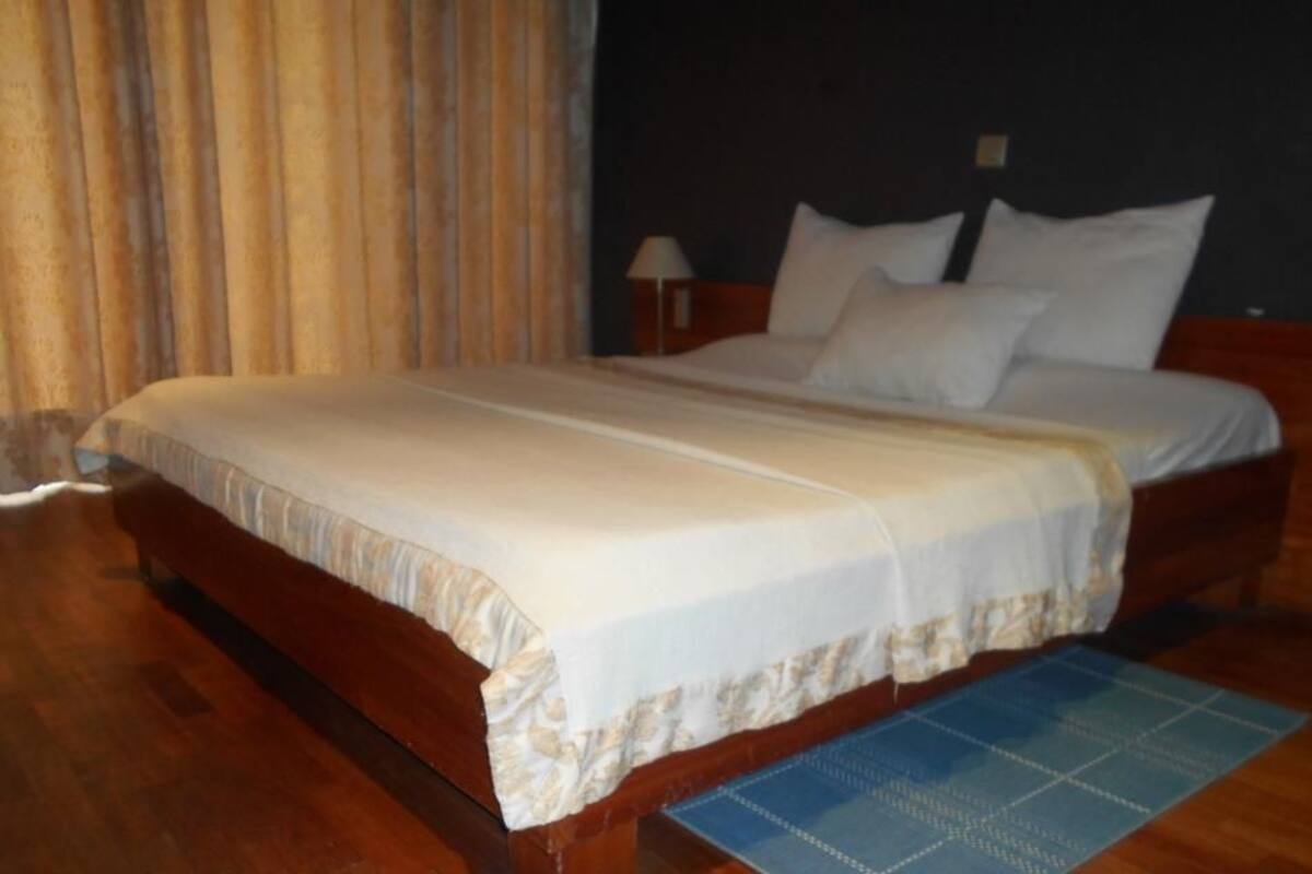 A neatly made bed with a white bedspread and pillows, a wooden headboard, and a blue area rug on a wooden floor.