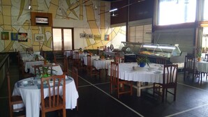 A restaurant with multiple tables and chairs, a buffet area, and a mural on the wall. - Hostellerie De La Sanaga (Edea)