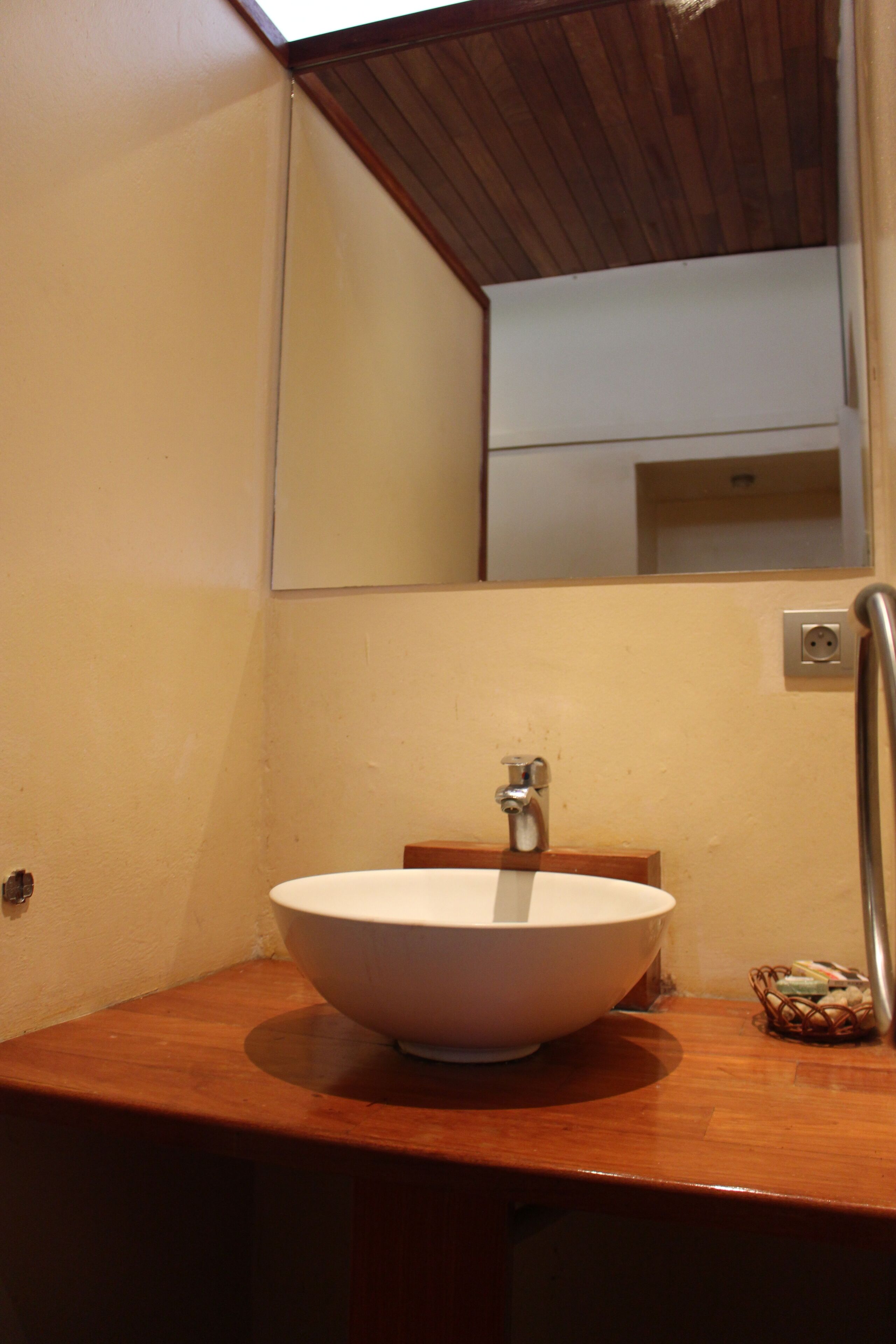Un baño con tocador de madera, lavamanos blanco y espejo arriba.