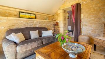 Una sala de estar acogedora con pared de piedra, un sofá marrón, una mesa de centro de madera y un tazón colorido.