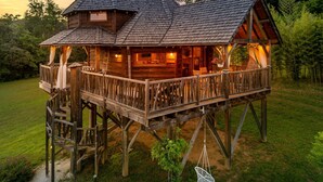 Une cabane en bois dotée d’un balcon et d’une terrasse, entourée de verdure.