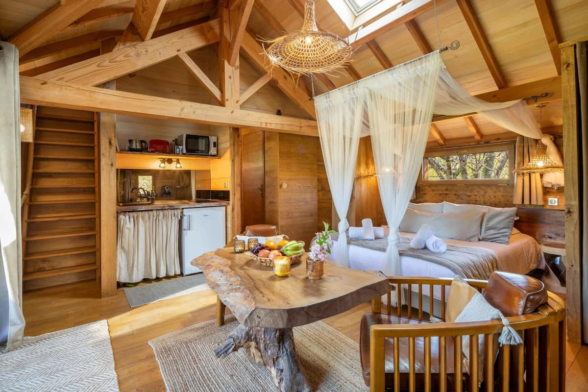 Een knus interieur van een blokhut met een houten eettafel, een bed met hemelbed en een kitchenette.