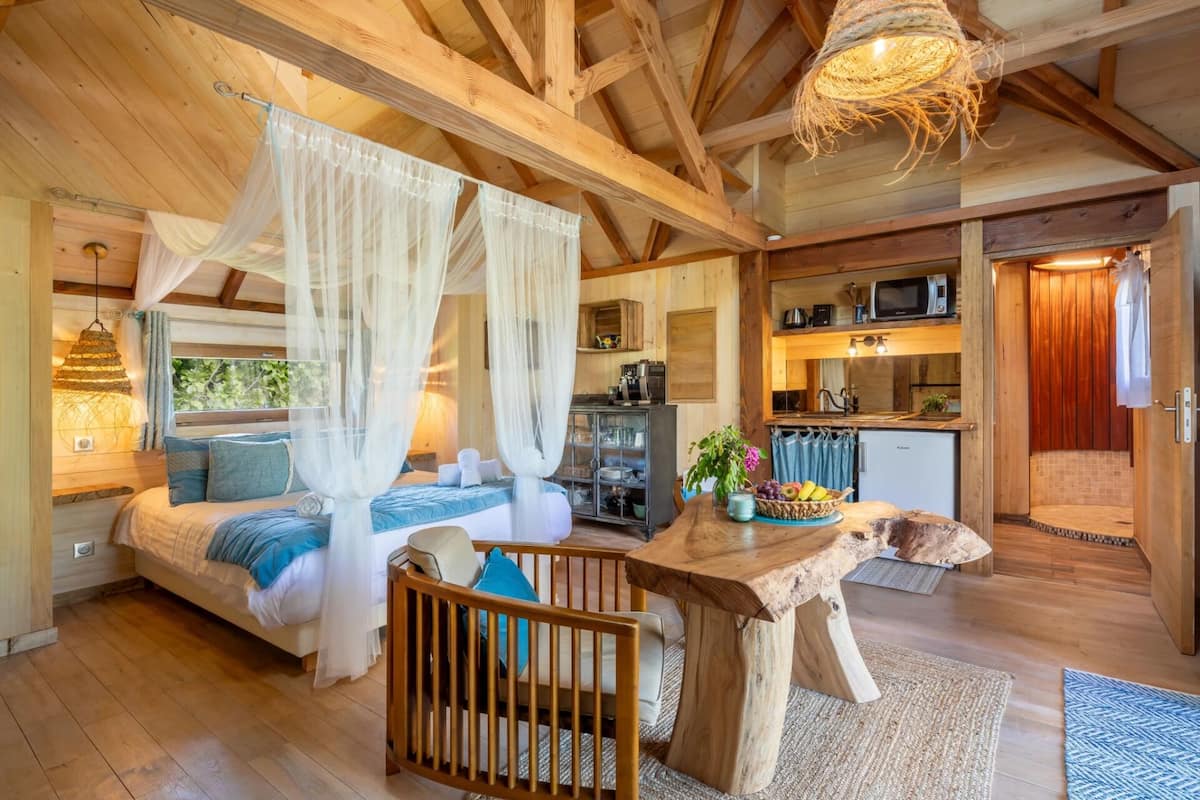 Een gezellige slaapkamer met een hemelbed, een houten eettafel en een kitchenette op de achtergrond.