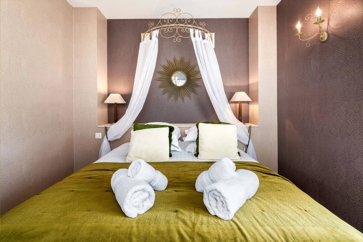 Een hotelkamer met een hemelbed, twee bedlampen, een decoratieve spiegel en een groene sprei.