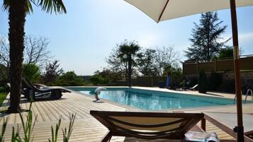 Una terraza de madera con sillones de descanso y una piscina.