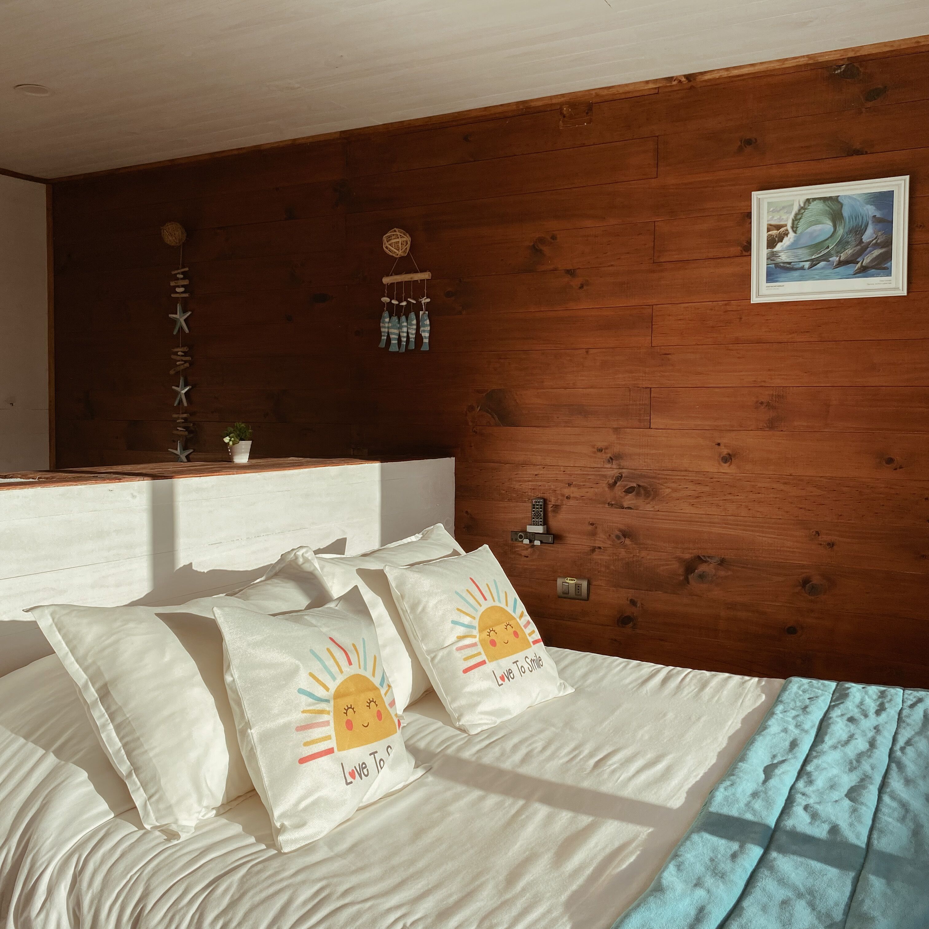 A bedroom with a wooden headboard, a bed with white bedding, and decorative pillows with a sun design.