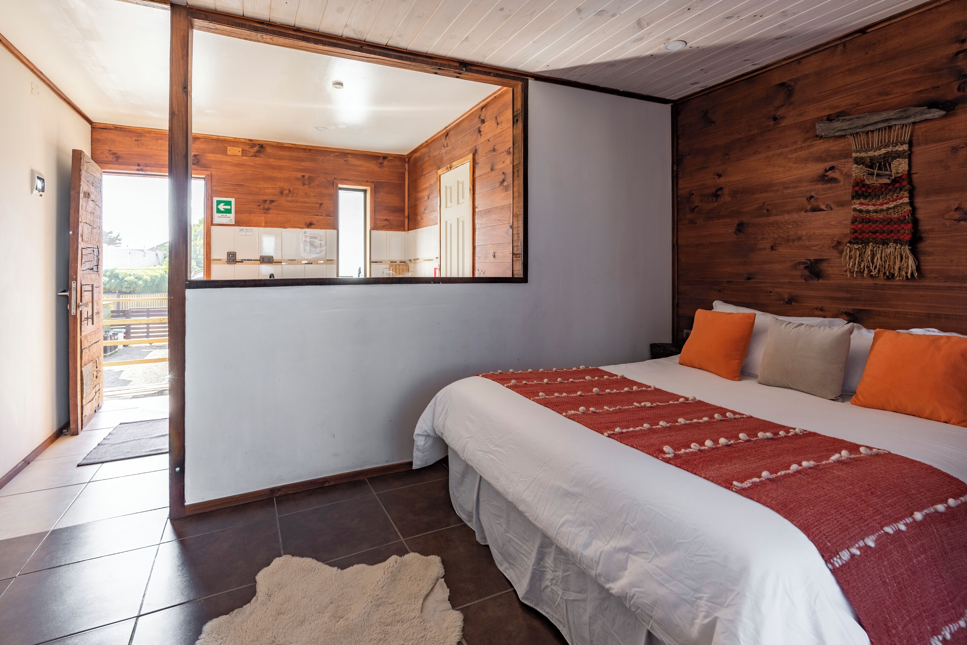 Une chambre avec un grand lit, un mur en bois, un miroir et une vue sur la cuisine.