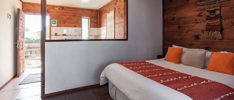 Une chambre avec un grand lit, un mur en bois, un miroir et une vue sur la cuisine.