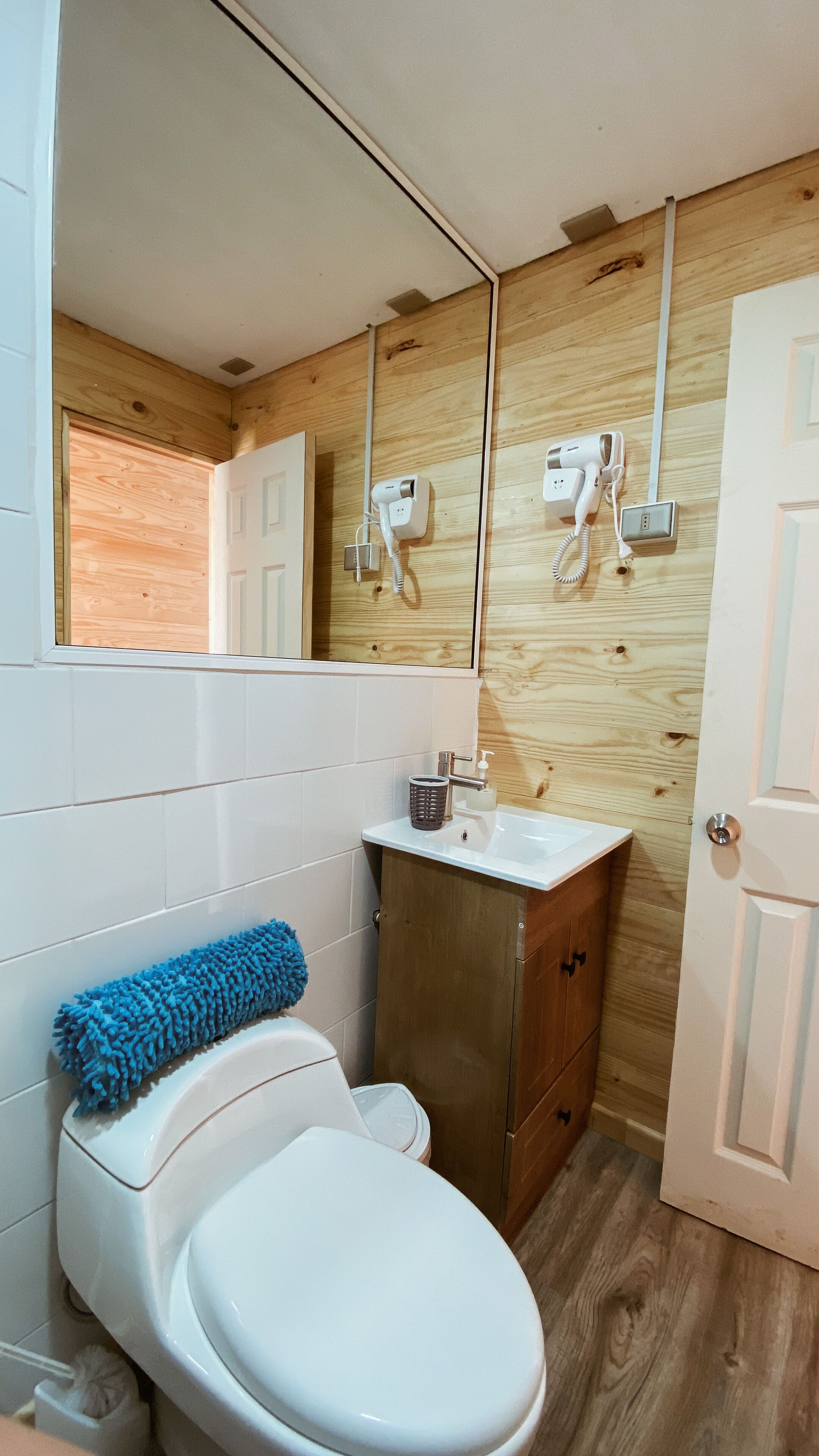 A compact bathroom with a white toilet, a sink with a soap dispenser, and a blue bath mat.
