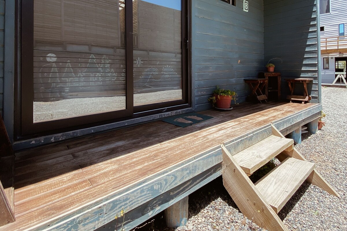 A building with large sliding glass doors, a wooden deck, and a small outdoor seating area with tables and chairs.