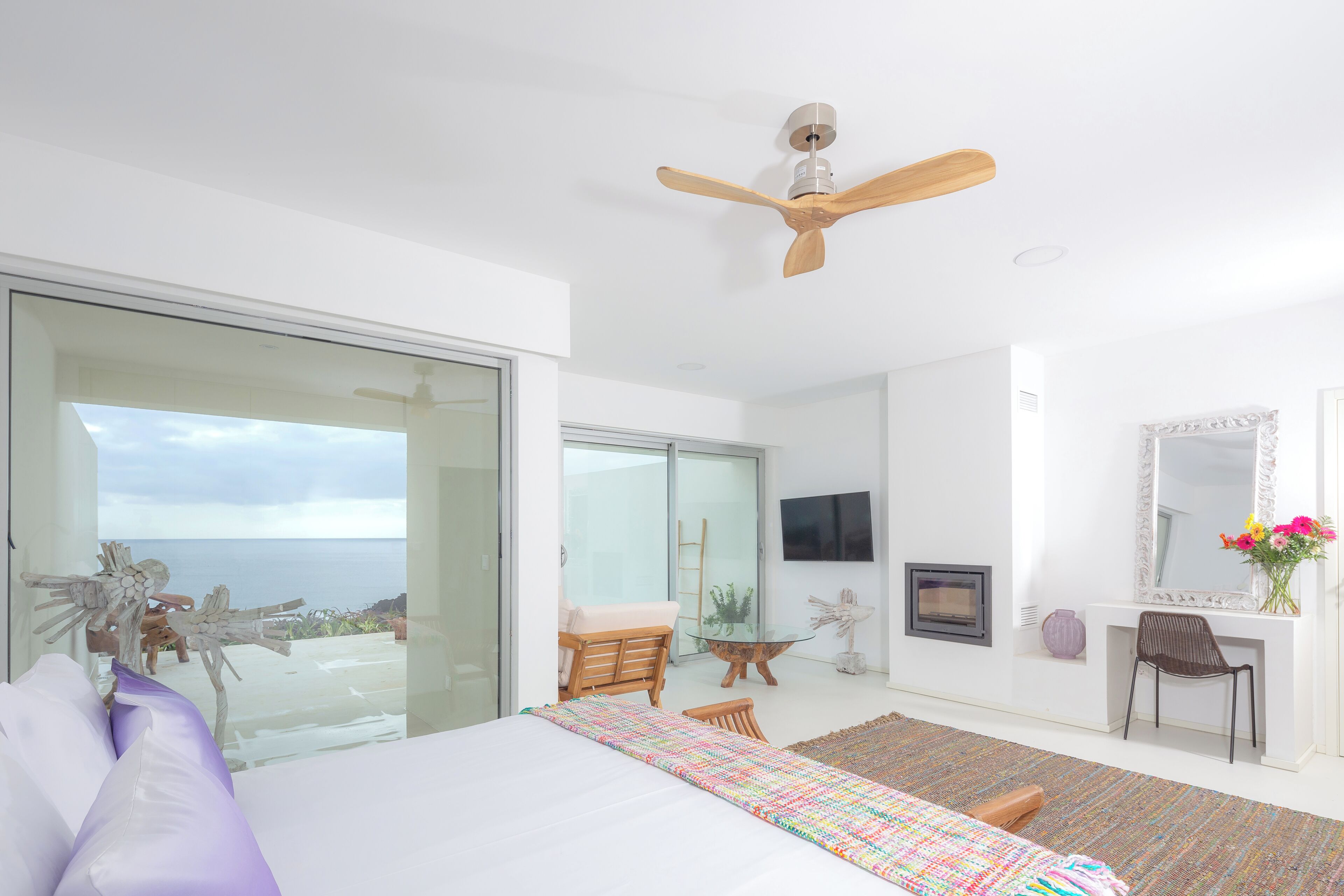A bedroom with a bed, a desk, a chair, a television, and a view of the ocean.
