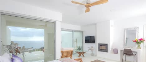A bedroom with a bed, a desk, a chair, a television, and a view of the ocean.