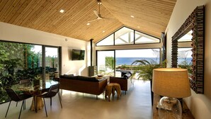 Ein modernes Interieur mit einem Glastisch, Sofas, einem Deckenventilator und Meerblick.