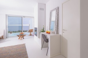 Une chambre moderne dotée d’une porte vitrée donnant sur un balcon, d’un bureau blanc avec une chaise et d’un grand miroir.