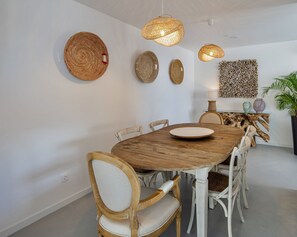 A dining area with a round wooden table, white upholstered chairs, woven wall hangings, and pendant lights. - Sul Villas & Spa (Lagoa)