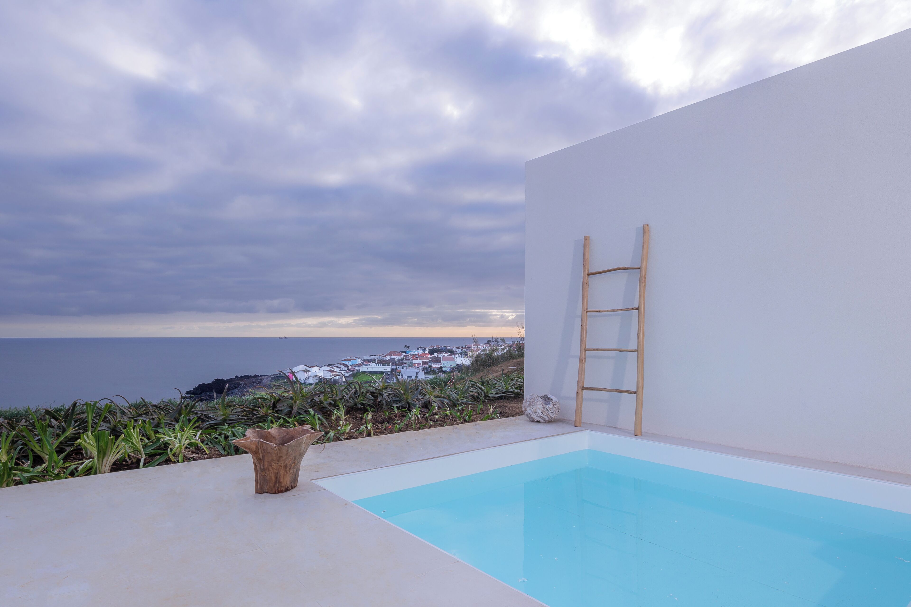 A modern outdoor pool area with a clear view of the sea and a white wall.
