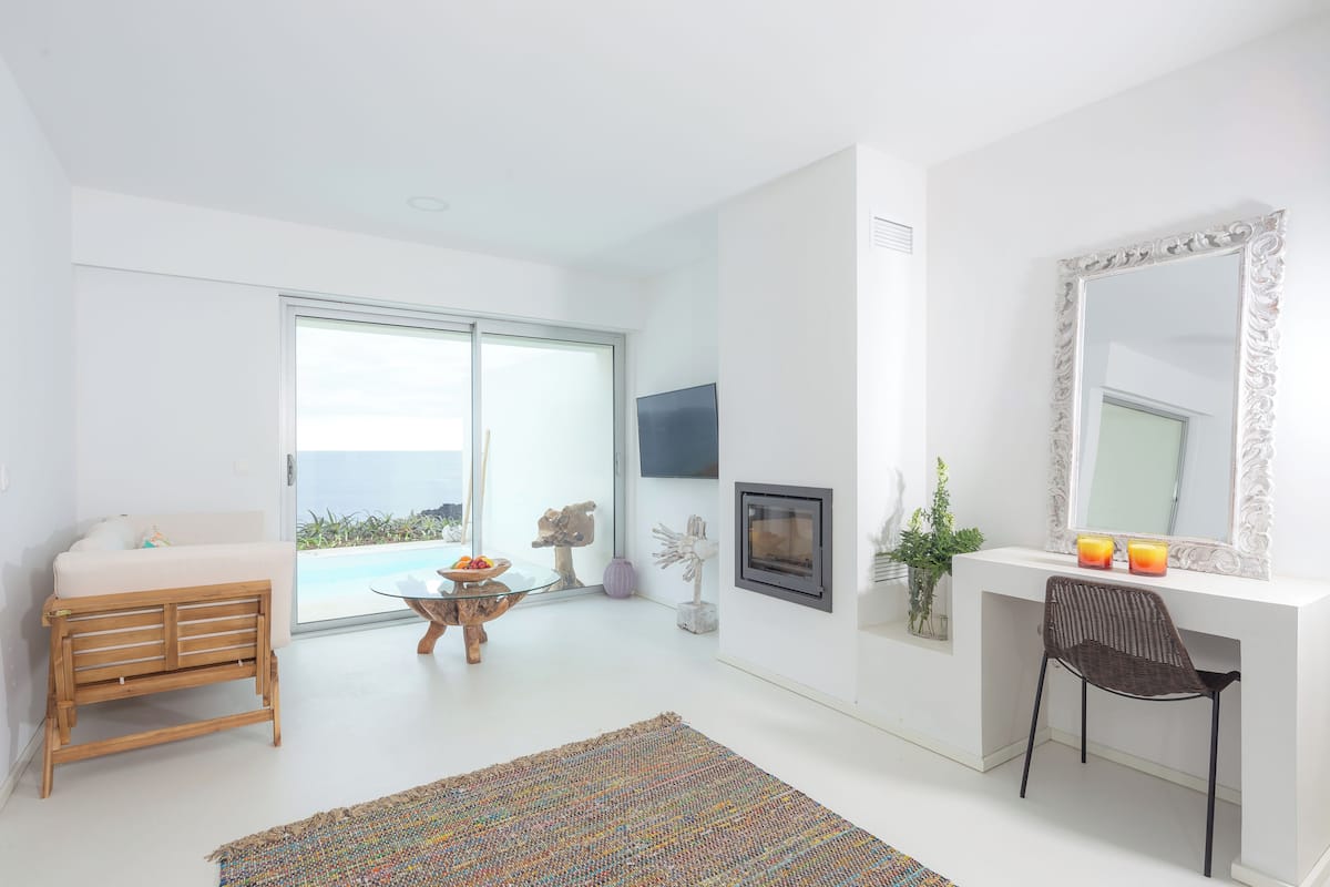 A modern room with a sofa, a dining table, a chair, a fireplace, and a large window.