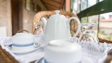 Un plateau sur lequel se trouvent une théière blanche, une tasse et un sucrier, posé sur une table en osier ornée d’une nappe en dentelle.
