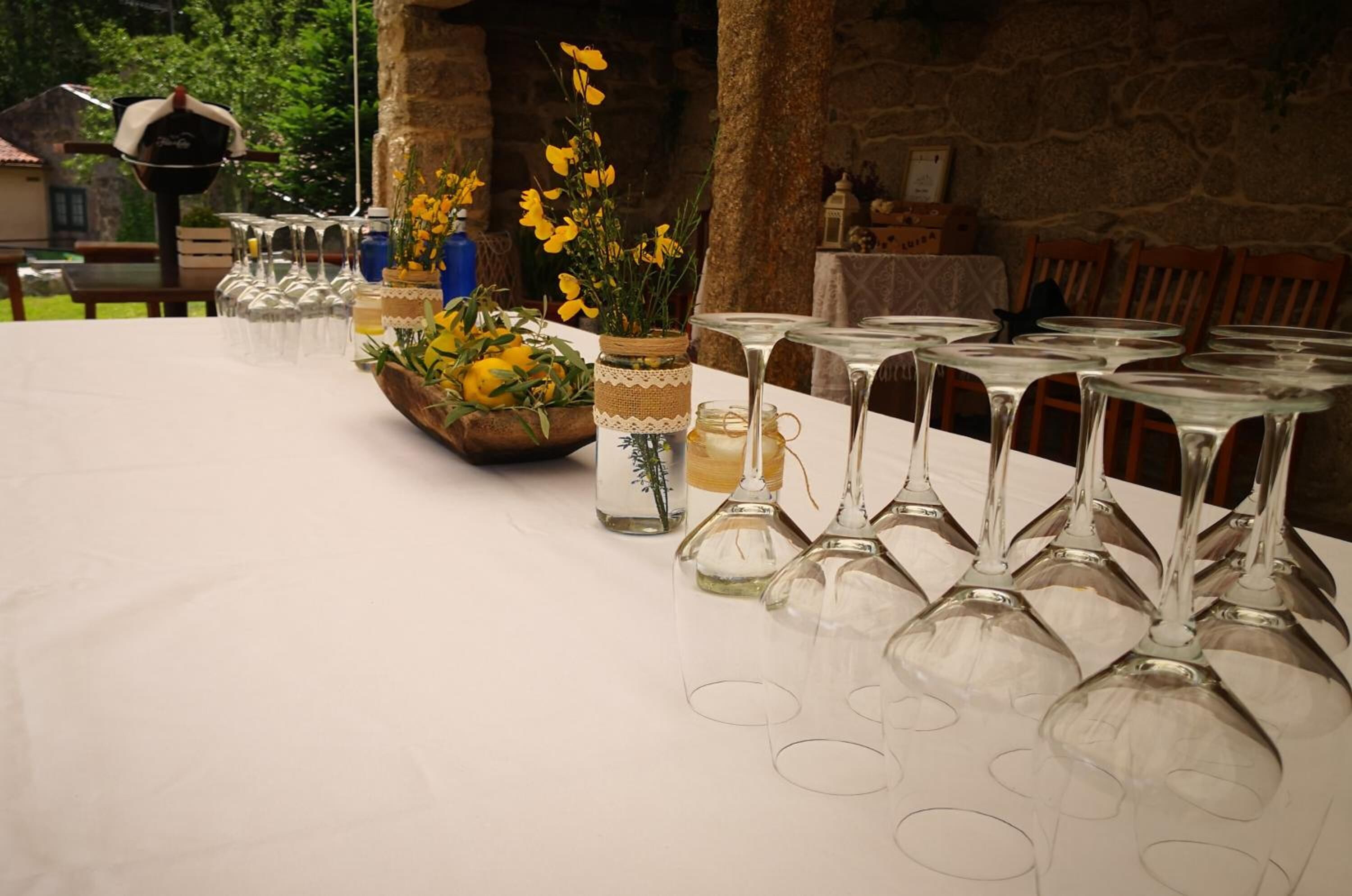 Una mesa dispuesta con copas de vino y jarrones con flores, frente a una pared de piedra.