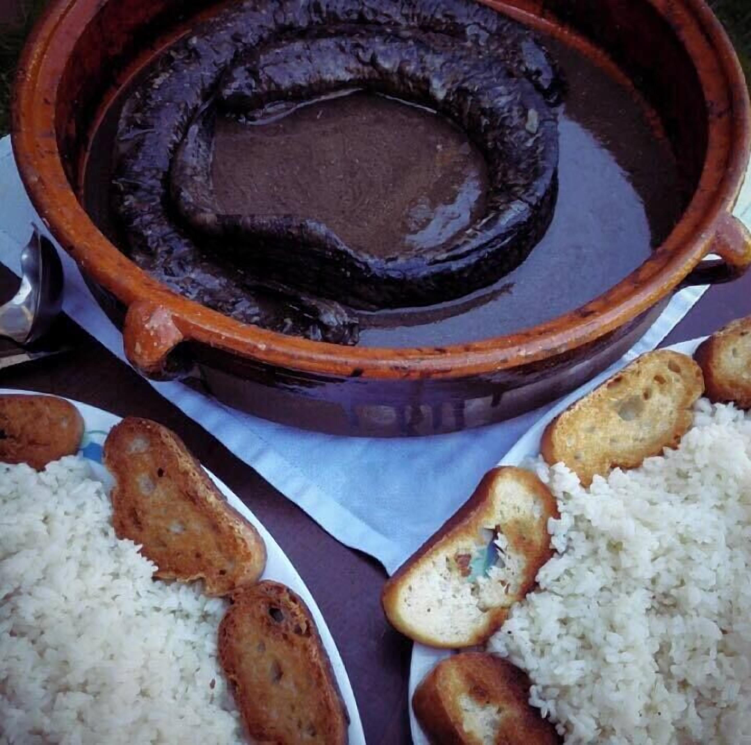 Una olla de barro con salsa oscura, acompañada de platos de arroz y pan tostado.