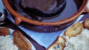 Una olla de barro con salsa oscura, acompañada de platos de arroz y pan tostado.