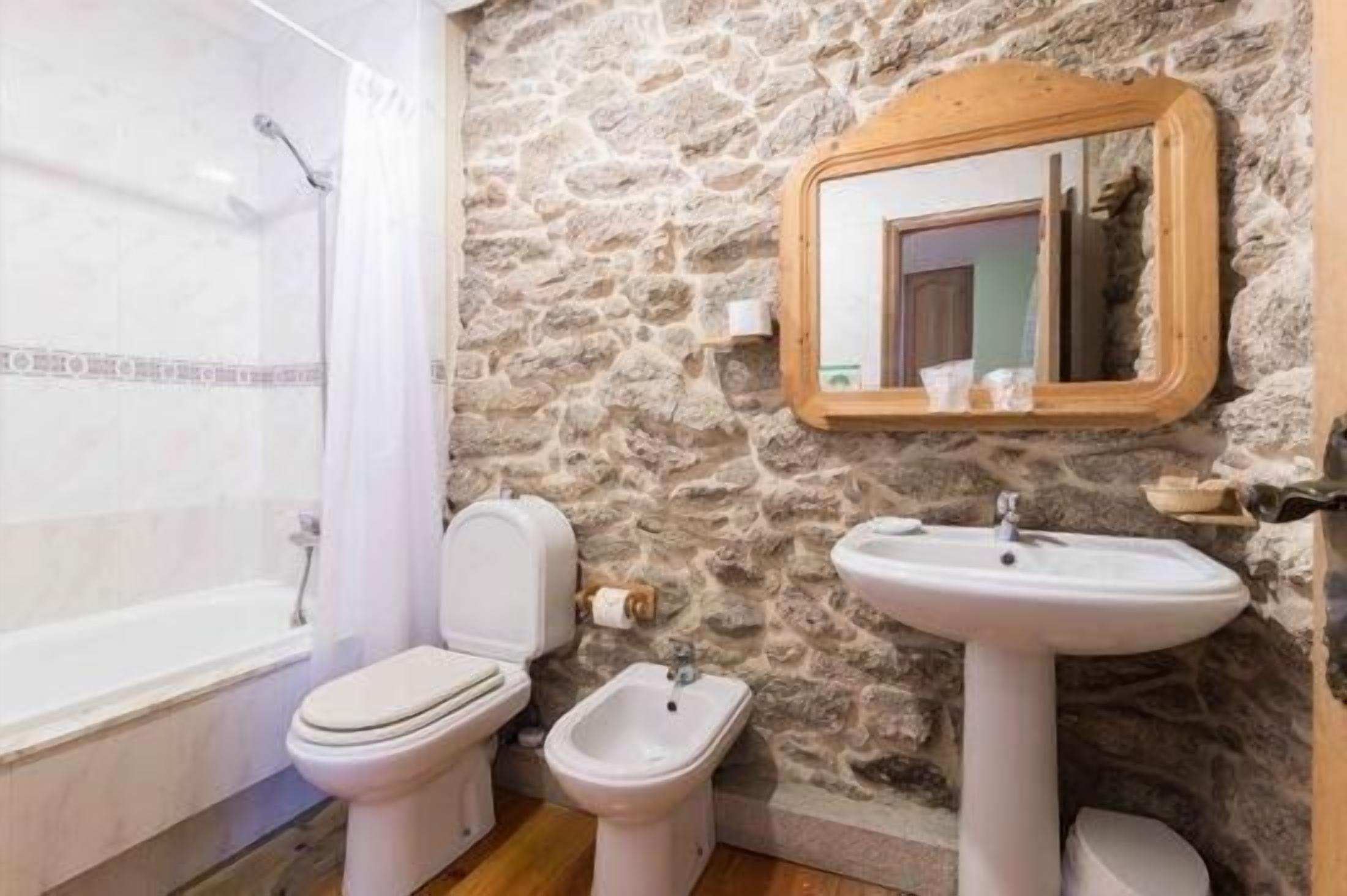 Uma casa de banho com parede de pedra, banheira, sanita, bidé e lavatório.