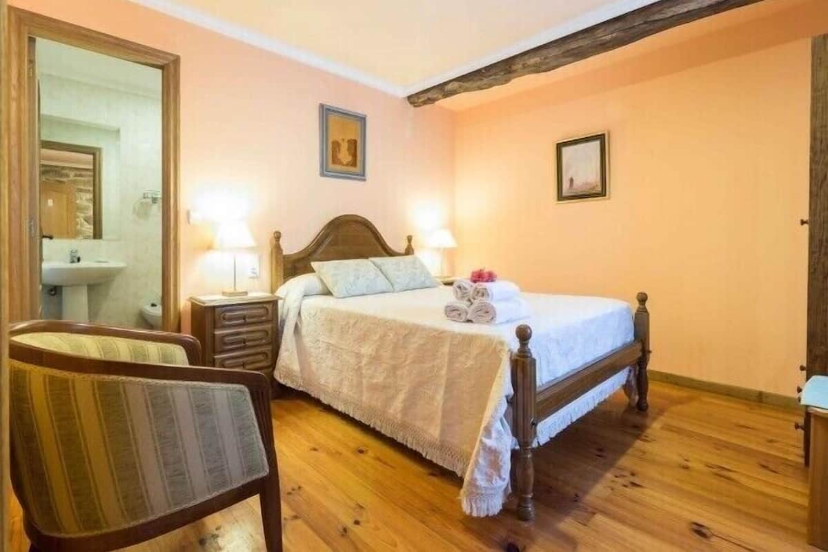 A bedroom with a wooden bed, two bedside tables with lamps, a chair, and a mirror.
