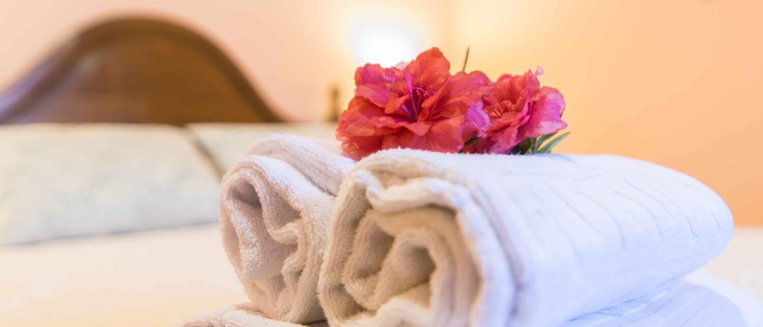 A neatly folded white towel with a pink flower on a bed.