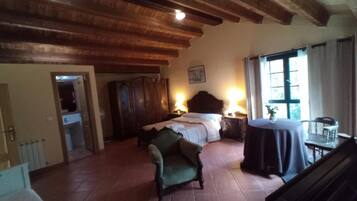A bedroom with a large bed, a green armchair, a wooden wardrobe, and a small table with a lamp.