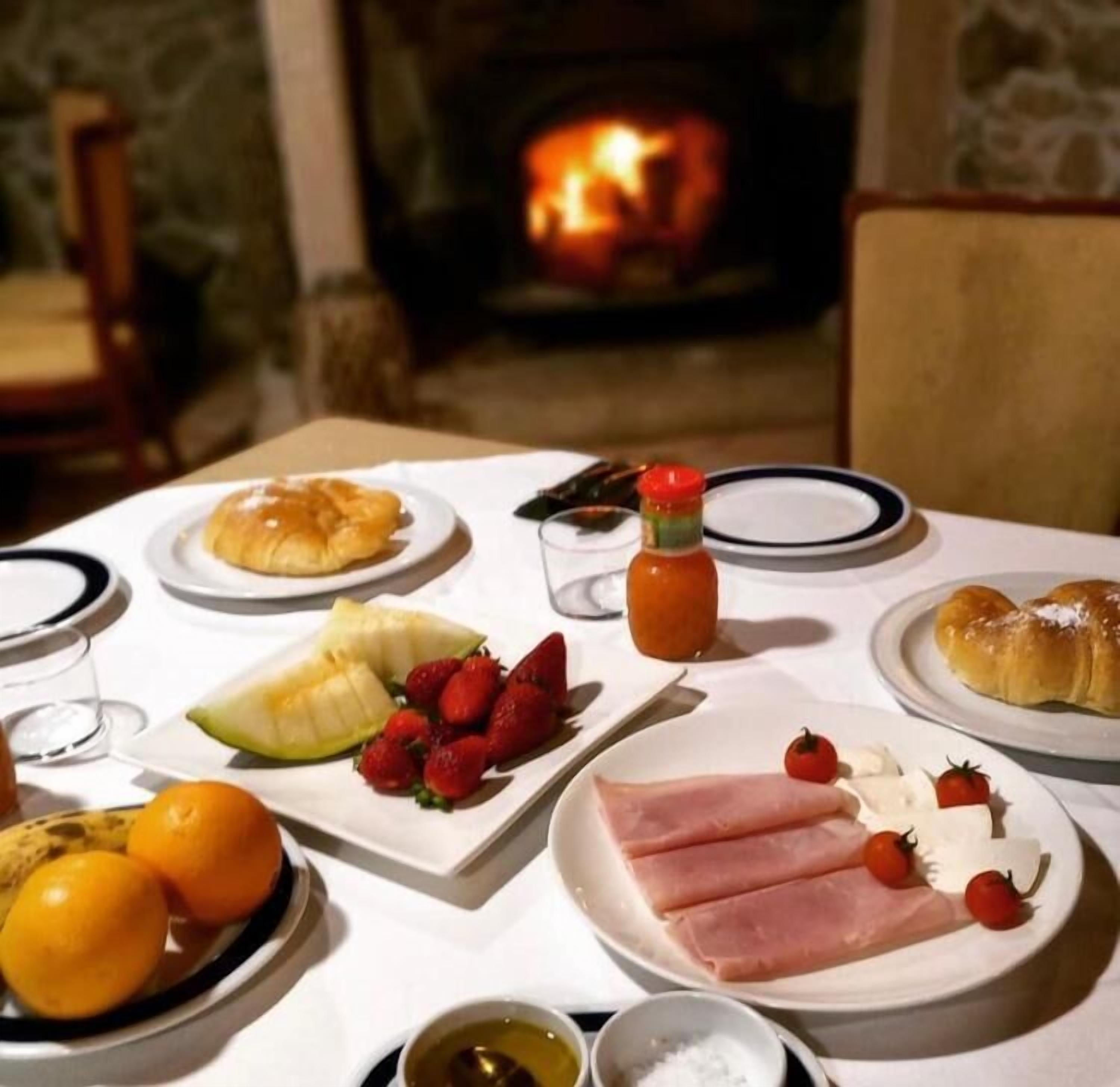 Una mesa lista para el desayuno, con platos de comida, una botella de salsa y una chimenea al fondo.