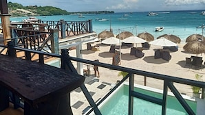 A beachside view with a pool, umbrellas, lounge chairs, and a wooden deck. - The Beach Huts Lembongan (Lembongan Island)
