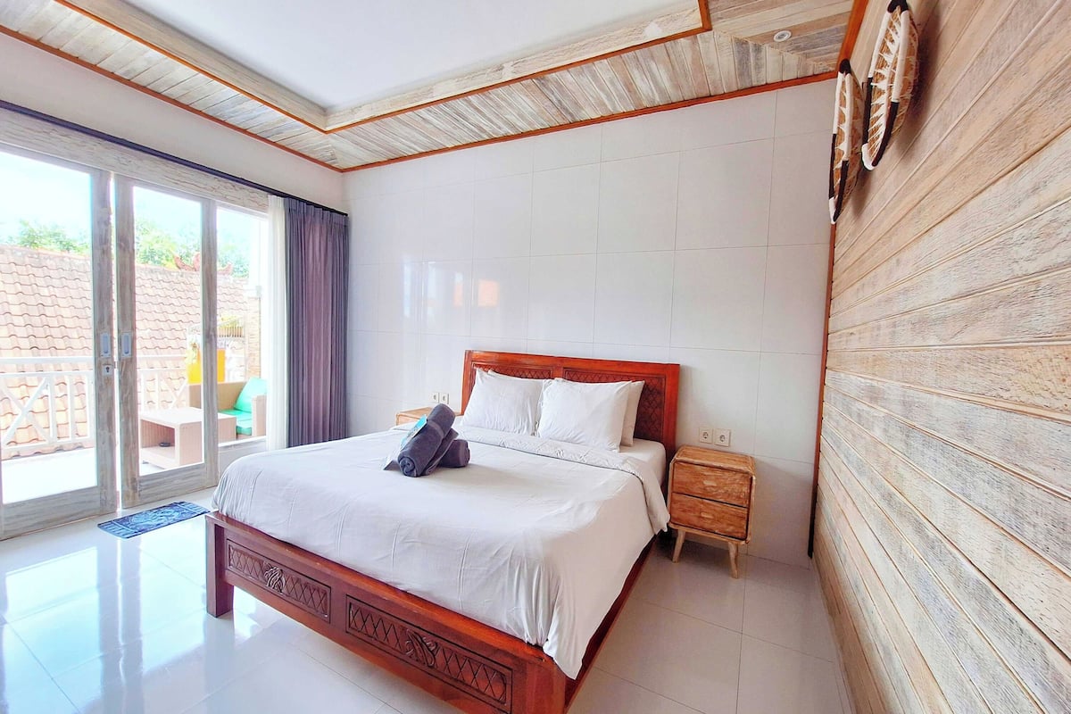 A bedroom with a wooden bed, a nightstand, and a view through a sliding glass door to an outdoor area.