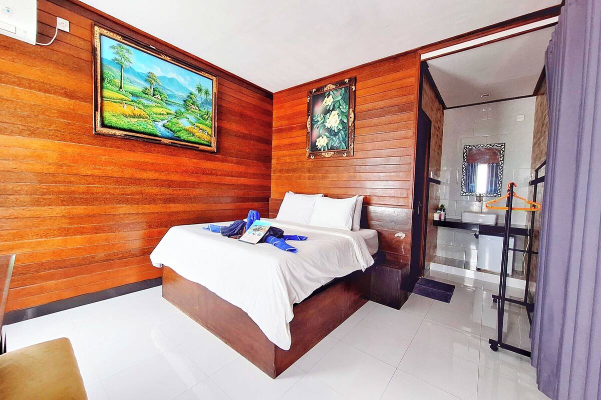 A bedroom with a wooden wall, a bed, a painting, and a view of a bathroom.
