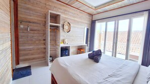 A bedroom with a large bed, wooden panel walls, a built-in desk, and a view of the outside. - The Beach Huts Lembongan (Lembongan Island)