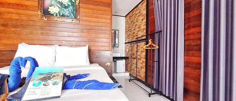 Une chambre d’hôtel avec des lambris en bois, un lit avec du linge de maison blanc, une œuvre d’art florale encadrée, une serviette bleue et une brochure posée sur le lit.