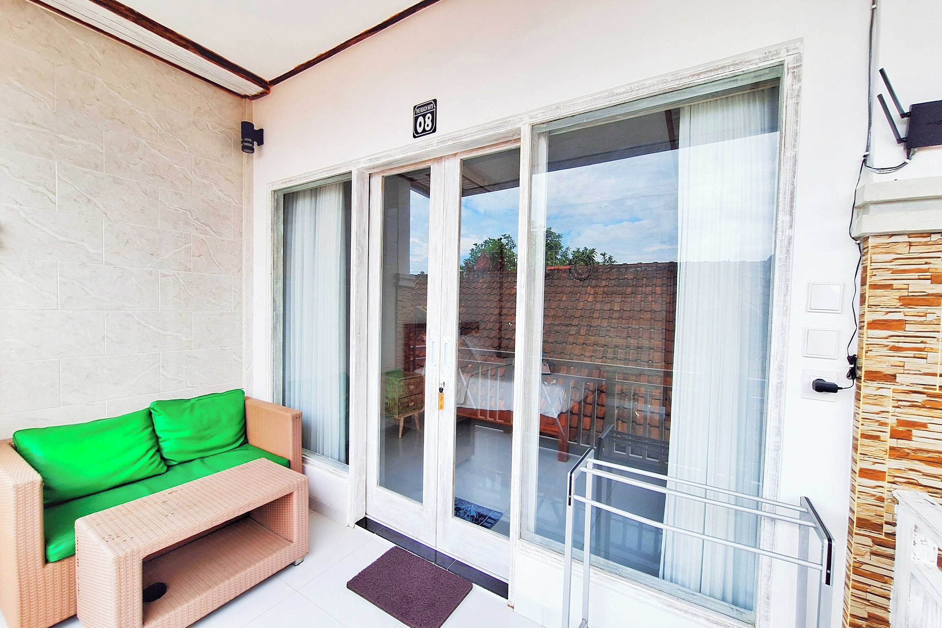 Ein Balkon mit einer Rattan-Couch, einer Glastür, die zu einer Terrasse führt, und einer Steinsäule.