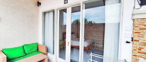 A balcony with a wicker sofa, a glass door leading to a patio, and a stone wall.