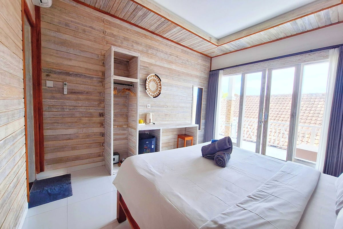 A bedroom with a large bed, wooden panel walls, a built-in desk, and a view of the outside.