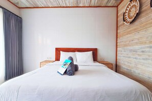A hotel room with a large bed, wooden headboard, white bedding, and a wall clock. - The Beach Huts Lembongan (Lembongan Island)