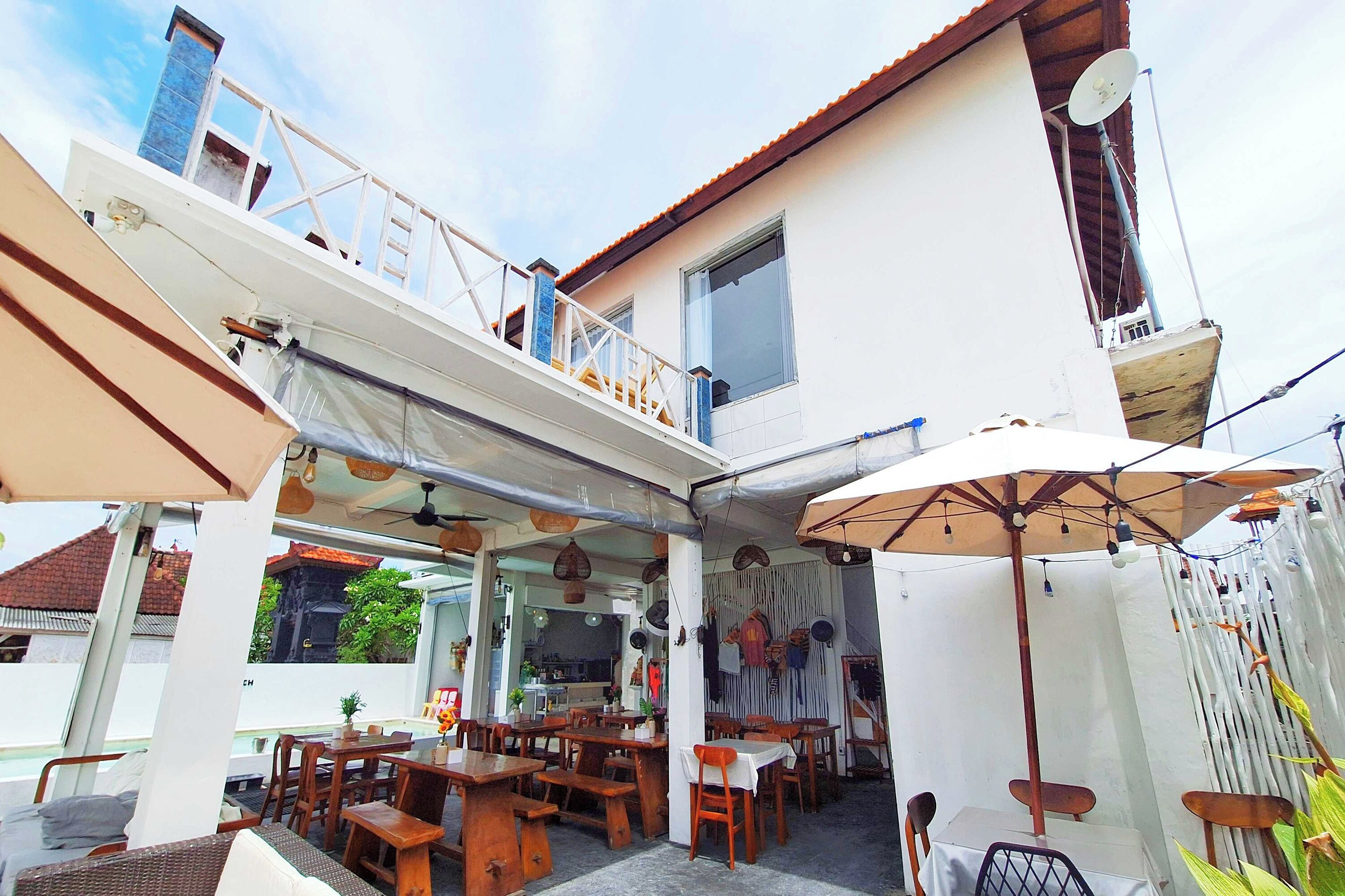 An outdoor dining area with wooden tables and chairs, umbrellas, and a view of the building's interior.