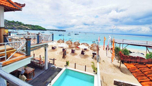 A beachside view with a pool, umbrellas, and lounge chairs. - The Beach Huts Lembongan (Lembongan Island)