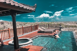 Un área de piscina con muelle de madera, sillas de descanso y un jacuzzi.