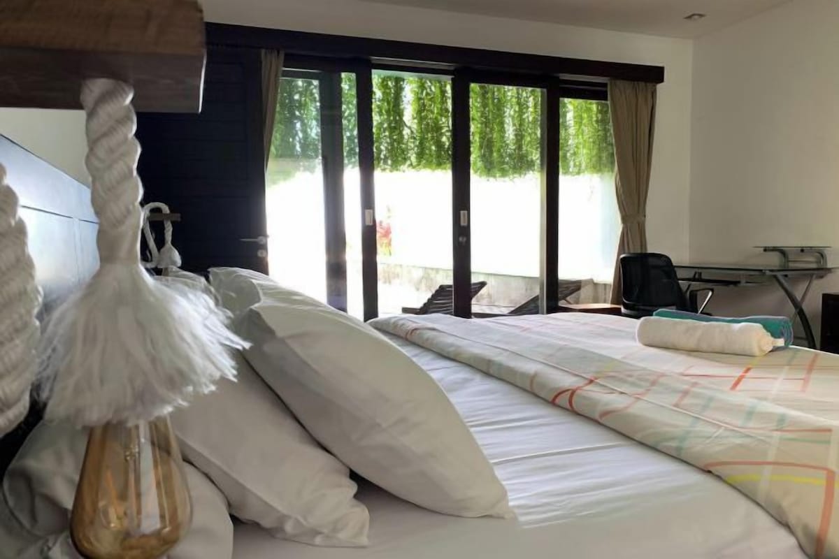 Habitación de hotel con una cama grande, un escritorio y vistas a zonas verdes a través de las ventanas.
