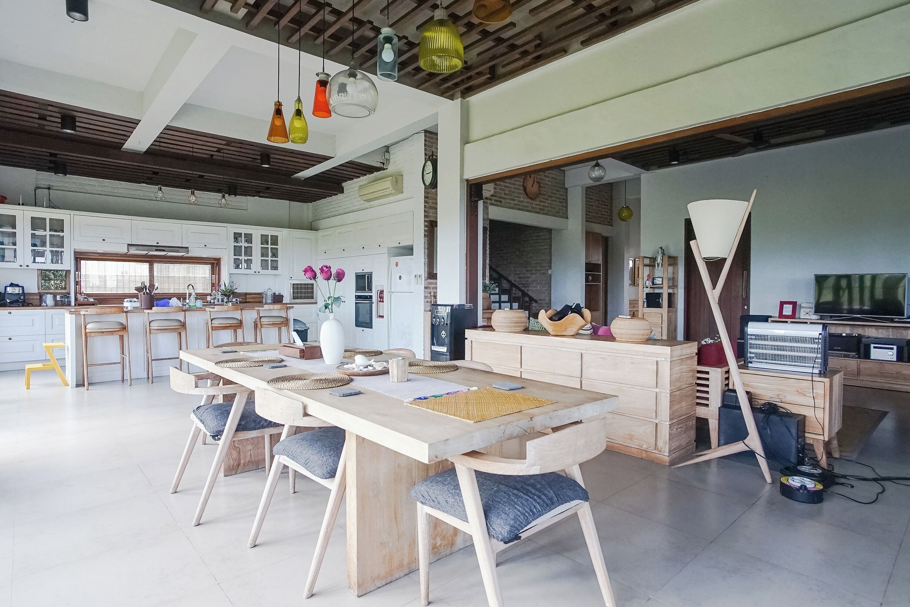 A spacious kitchen with wooden cabinets, a dining area with a large table and chairs, and a modern ceiling with pendant lights.
