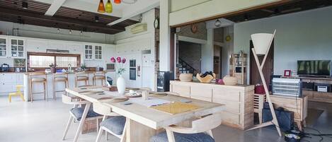 A spacious kitchen with wooden cabinets, a dining area with a large table and chairs, and a modern ceiling with pendant lights.